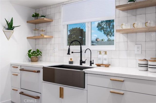 kitchen with light countertops, tasteful backsplash, open shelves, and a sink