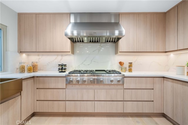 kitchen with tasteful backsplash, stainless steel gas stovetop, wall chimney range hood, and light brown cabinetry