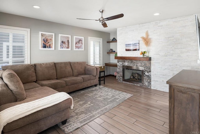 living area featuring recessed lighting, light wood-style flooring, a ceiling fan, and a stone fireplace