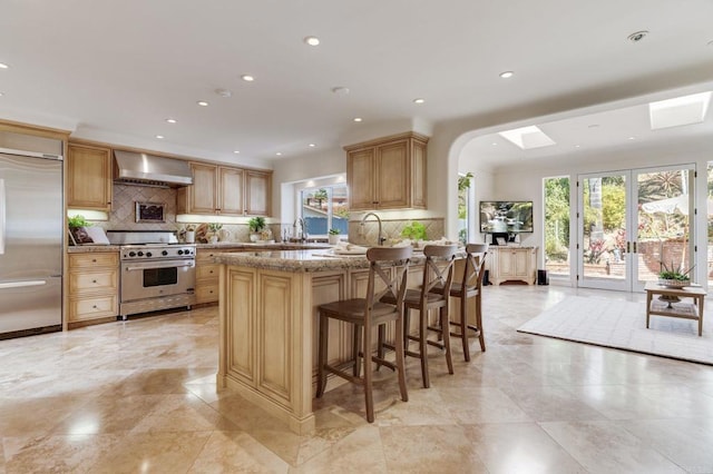 kitchen featuring recessed lighting, a kitchen breakfast bar, appliances with stainless steel finishes, wall chimney exhaust hood, and tasteful backsplash