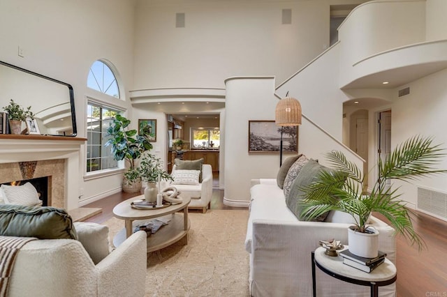 living area with a towering ceiling, visible vents, wood finished floors, and a high end fireplace