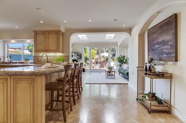 kitchen featuring arched walkways, stone counters, light brown cabinets, a sink, and tasteful backsplash