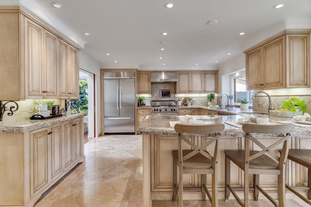 kitchen featuring built in refrigerator, light brown cabinets, range, and light stone countertops