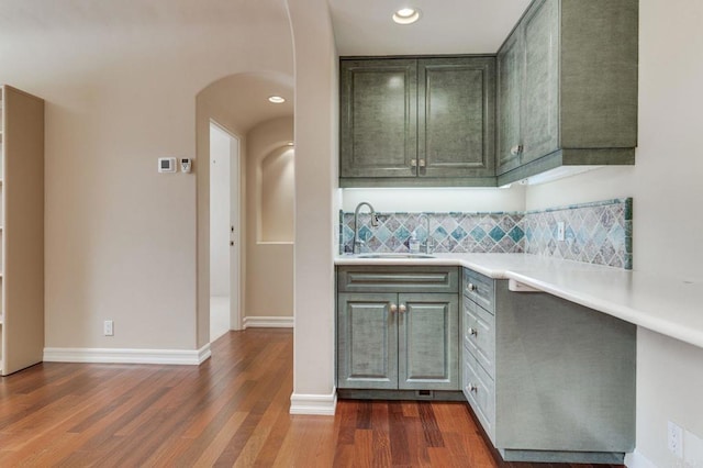 kitchen with arched walkways, dark wood-type flooring, a sink, light countertops, and backsplash