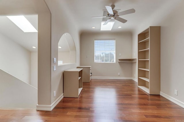 unfurnished room featuring a skylight, baseboards, dark wood finished floors, and recessed lighting