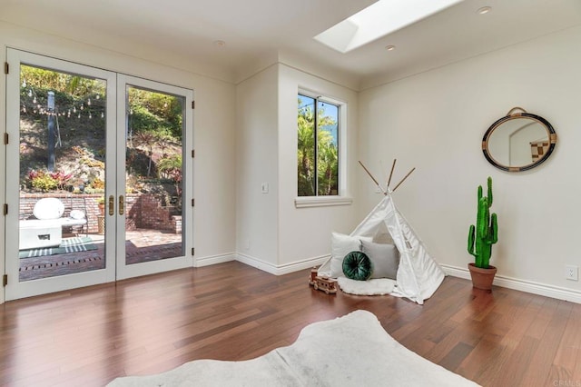 recreation room featuring a skylight, french doors, baseboards, and wood finished floors