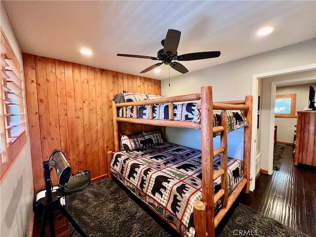 bedroom with wood walls, ceiling fan, baseboards, and dark wood-style flooring