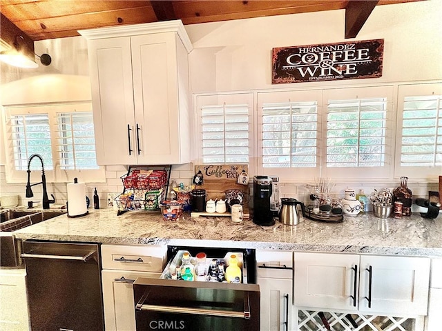 kitchen with white cabinets, dishwasher, light stone counters, a sink, and backsplash