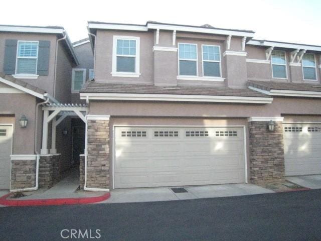 townhome / multi-family property with stone siding, stucco siding, and a garage