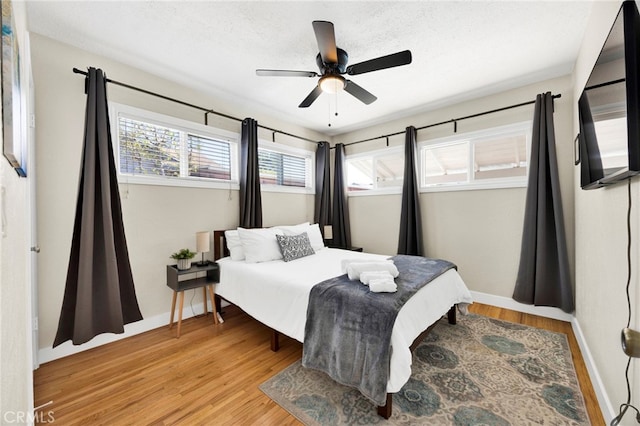 bedroom featuring a ceiling fan, light wood-type flooring, a textured ceiling, and baseboards