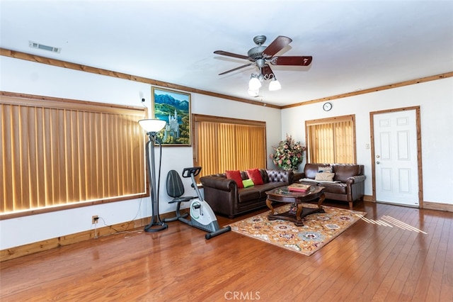 living room with wood-type flooring, visible vents, ornamental molding, ceiling fan, and baseboards