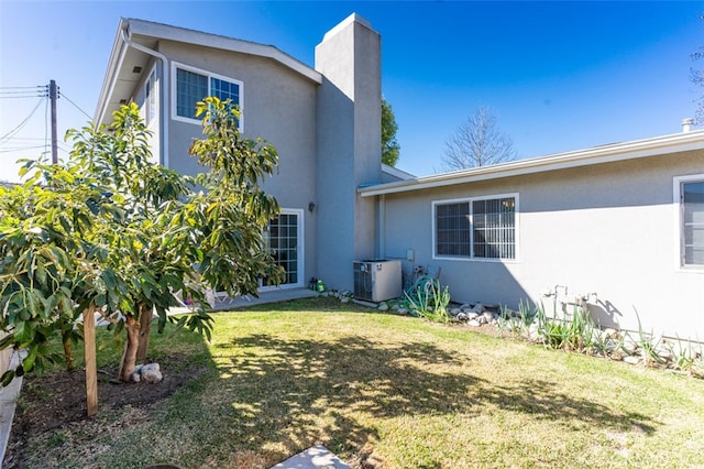 rear view of property featuring a chimney, a lawn, stucco siding, and central air condition unit