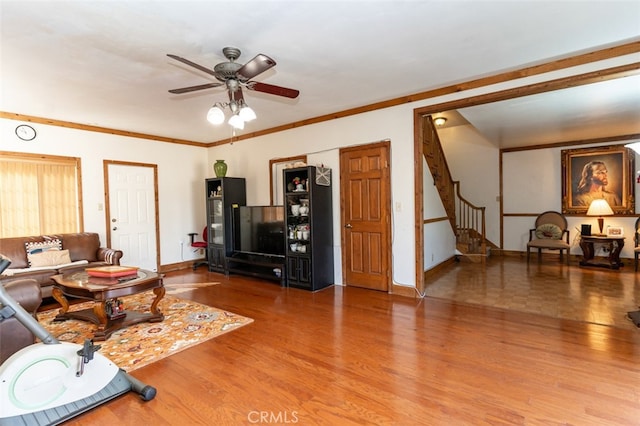 living room with a ceiling fan, crown molding, stairway, and wood finished floors