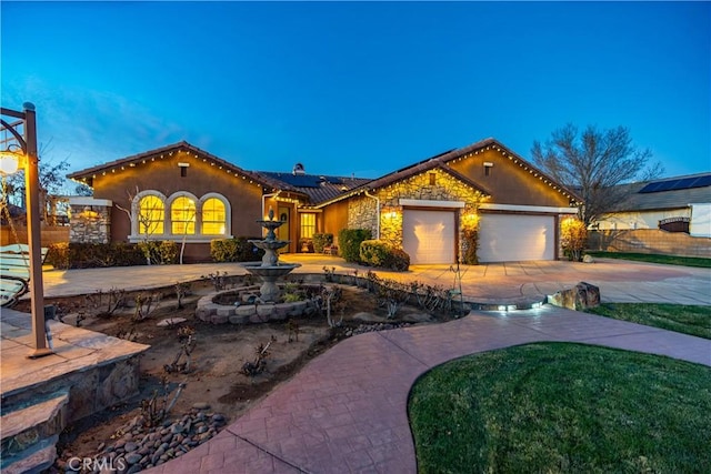 mediterranean / spanish house with stucco siding, concrete driveway, an attached garage, fence, and stone siding