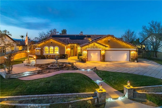 mediterranean / spanish-style home featuring driveway, an attached garage, roof mounted solar panels, and a front yard