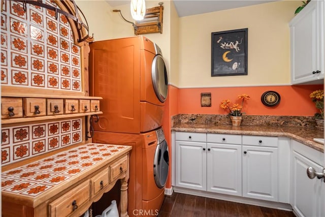 clothes washing area with dark wood-type flooring, stacked washer and clothes dryer, and cabinet space