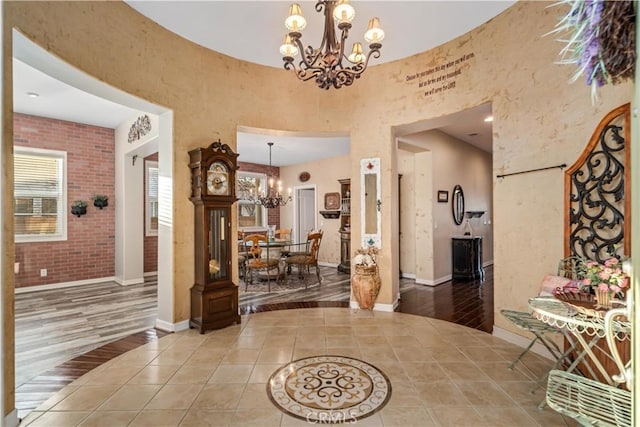 foyer entrance featuring an inviting chandelier, tile patterned flooring, brick wall, and baseboards