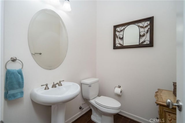 half bath with toilet, baseboards, and wood finished floors