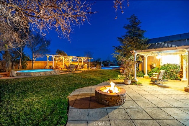 yard at night featuring an outdoor fire pit, a fenced in pool, and a patio