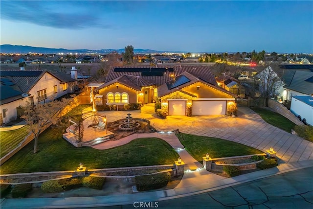 mediterranean / spanish home featuring decorative driveway, a yard, a mountain view, a garage, and a tiled roof