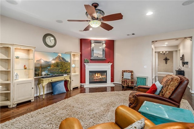 living area featuring dark wood-style floors, a glass covered fireplace, visible vents, and ceiling fan