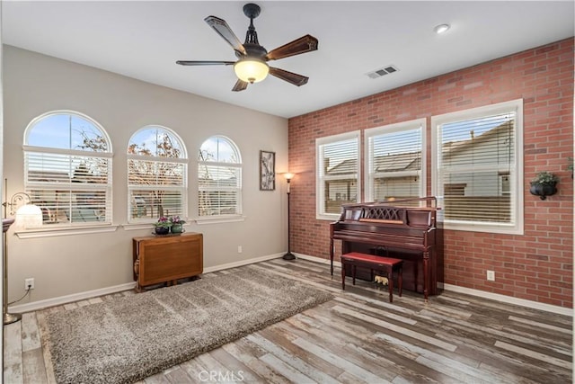 sitting room with visible vents, baseboards, a ceiling fan, brick wall, and wood finished floors