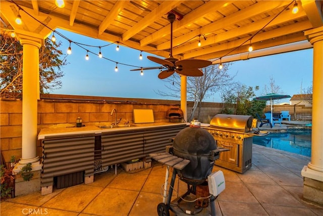 patio terrace at dusk with a fenced backyard, an outdoor kitchen, a sink, and a fenced in pool