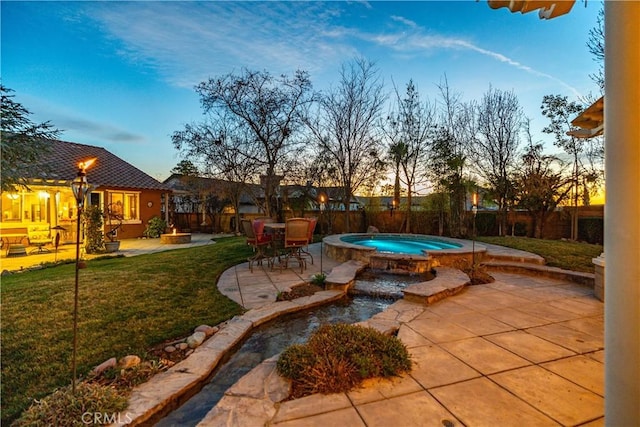 pool at dusk featuring an in ground hot tub, a yard, a patio, and a fenced backyard