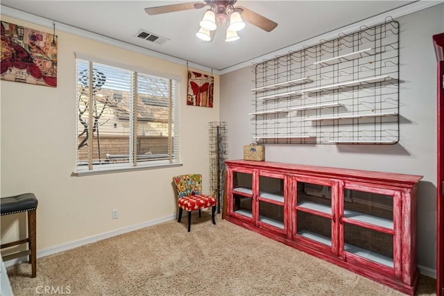 interior space featuring carpet floors, visible vents, baseboards, a ceiling fan, and crown molding