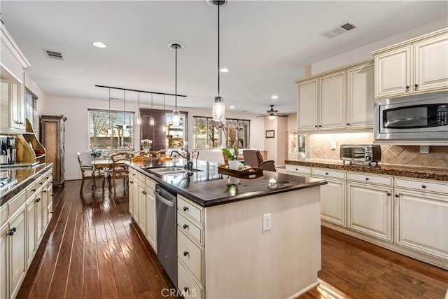 kitchen with cream cabinetry, decorative light fixtures, dark countertops, appliances with stainless steel finishes, and a sink