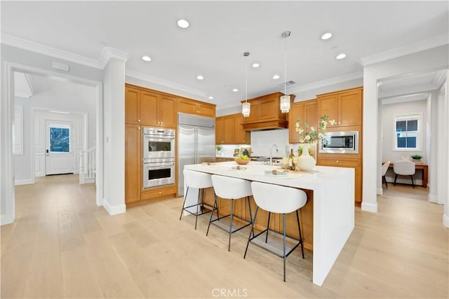 kitchen featuring decorative light fixtures, light countertops, a kitchen island with sink, built in appliances, and a kitchen breakfast bar