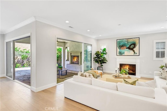 living room with ornamental molding, recessed lighting, a glass covered fireplace, and light wood-style floors