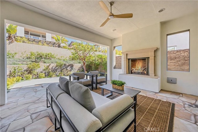 view of patio / terrace with a ceiling fan, fence, and an outdoor living space with a fireplace