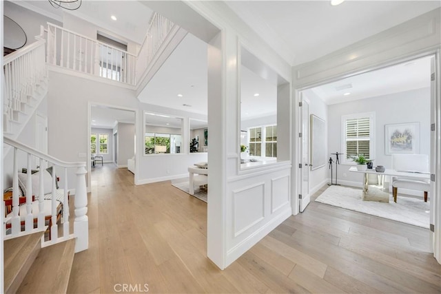 foyer with light wood-type flooring, crown molding, and stairs