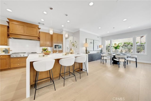 kitchen featuring brown cabinetry, a center island with sink, visible vents, and light countertops