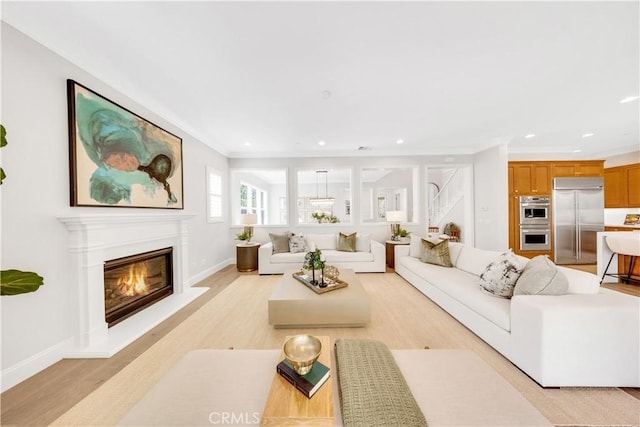 living room with light wood finished floors, baseboards, a glass covered fireplace, ornamental molding, and recessed lighting