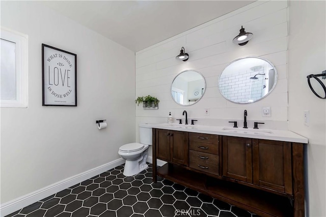 bathroom featuring toilet, double vanity, baseboards, and a sink