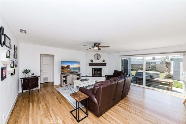 living area with a fireplace, visible vents, light wood-style floors, a ceiling fan, and baseboards