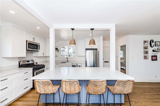 kitchen featuring stainless steel appliances, white cabinets, light countertops, a center island, and pendant lighting