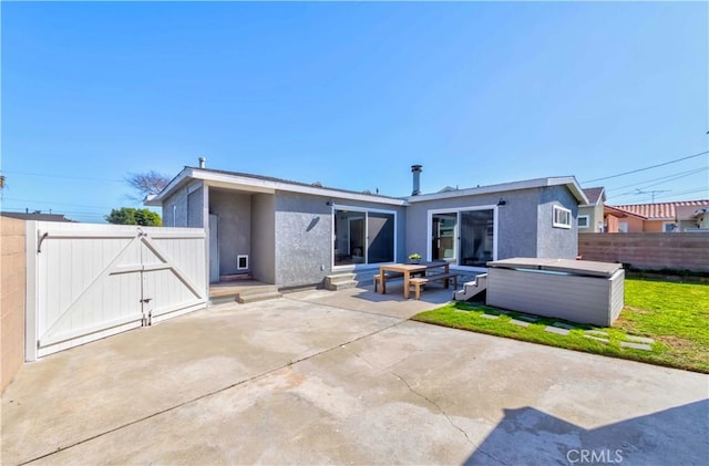 rear view of house with a patio, fence, a gate, stucco siding, and a hot tub