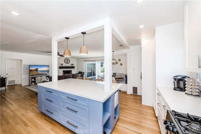 kitchen featuring a fireplace, open shelves, light countertops, open floor plan, and stainless steel gas range oven