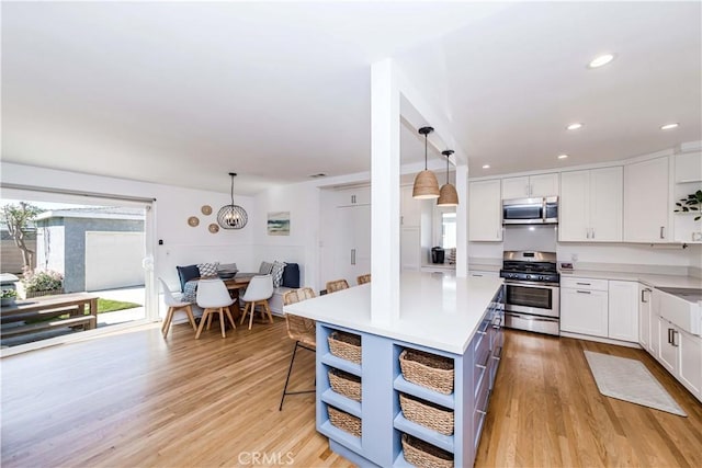 kitchen featuring a breakfast bar, light countertops, hanging light fixtures, appliances with stainless steel finishes, and white cabinets