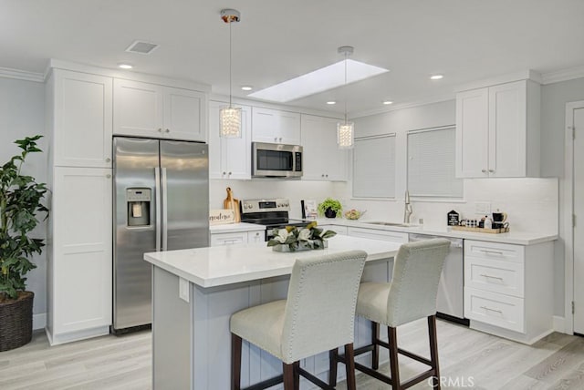 kitchen with white cabinets, stainless steel appliances, light countertops, pendant lighting, and a sink