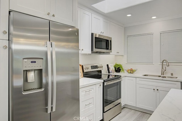 kitchen featuring light stone counters, stainless steel appliances, a sink, white cabinets, and tasteful backsplash