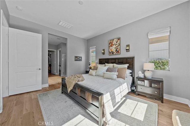 bedroom featuring light wood-style floors, multiple windows, baseboards, and a walk in closet