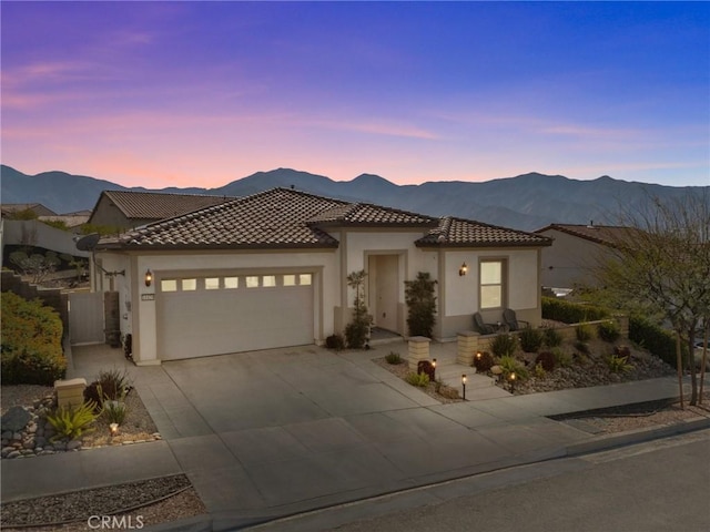 view of front of house with a tile roof, stucco siding, concrete driveway, an attached garage, and a mountain view