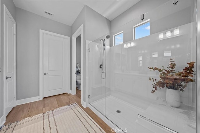 bathroom with toilet, wood finished floors, visible vents, baseboards, and a shower stall