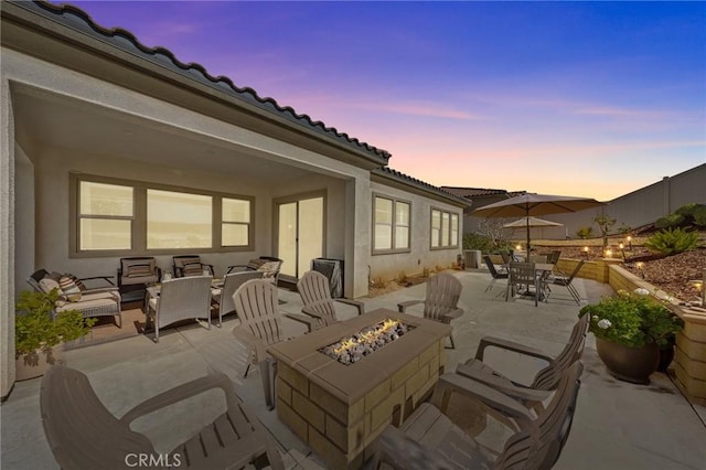 patio terrace at dusk featuring an outdoor fire pit and fence