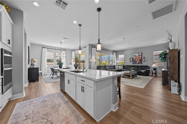 kitchen featuring an island with sink, visible vents, white cabinetry, and light countertops