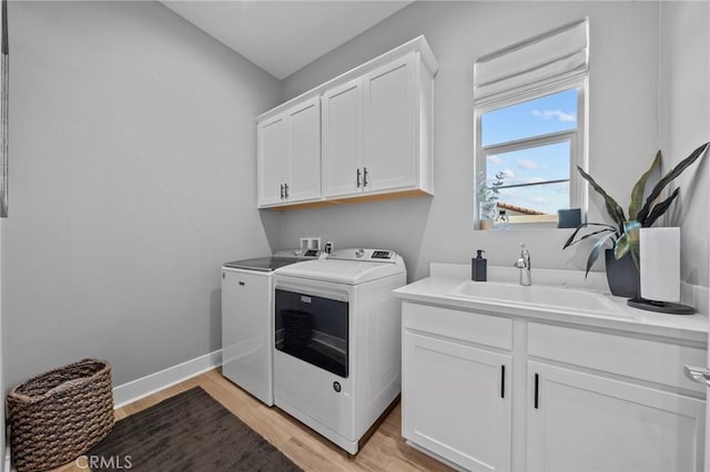 clothes washing area with washing machine and clothes dryer, cabinet space, a sink, light wood-type flooring, and baseboards